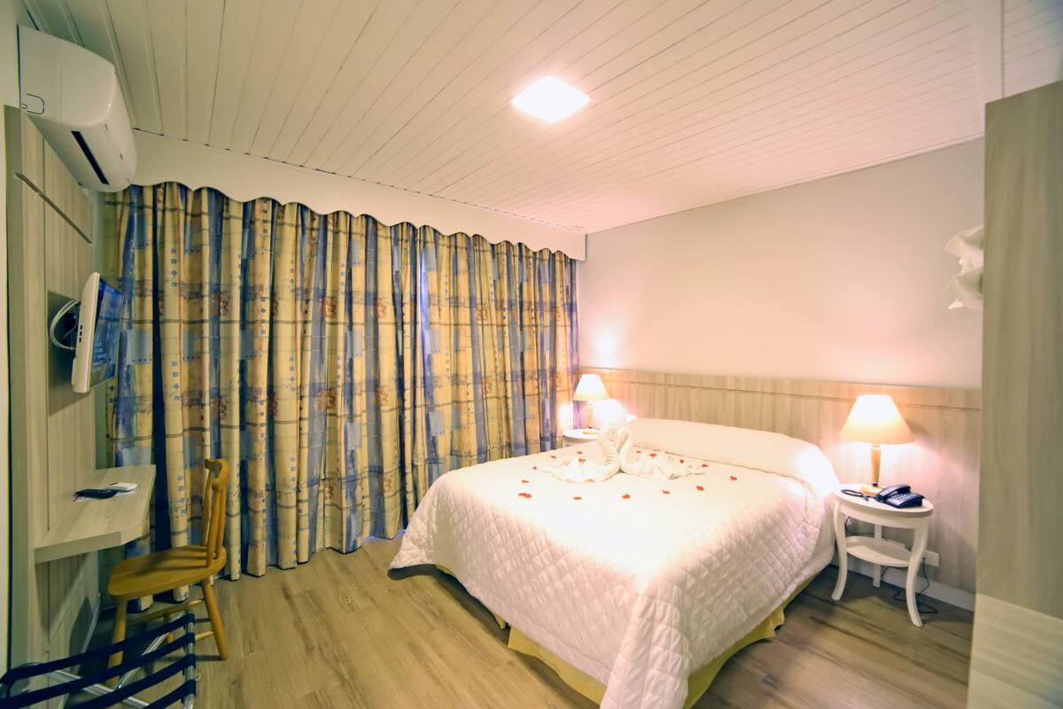 Une chambre d’hôtel comprenant un lit, deux lampes de chevet, une chaise, une petite table et un climatiseur fixé au mur.