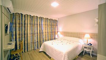 Quarto de hotel com cama, duas luminárias de cabeceira, uma cadeira, uma mesinha e ar condicionado fixado na parede.