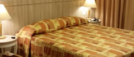 A hotel room with a large bed, two bedside lamps, a wooden headboard, a wooden desk, and a chair.
