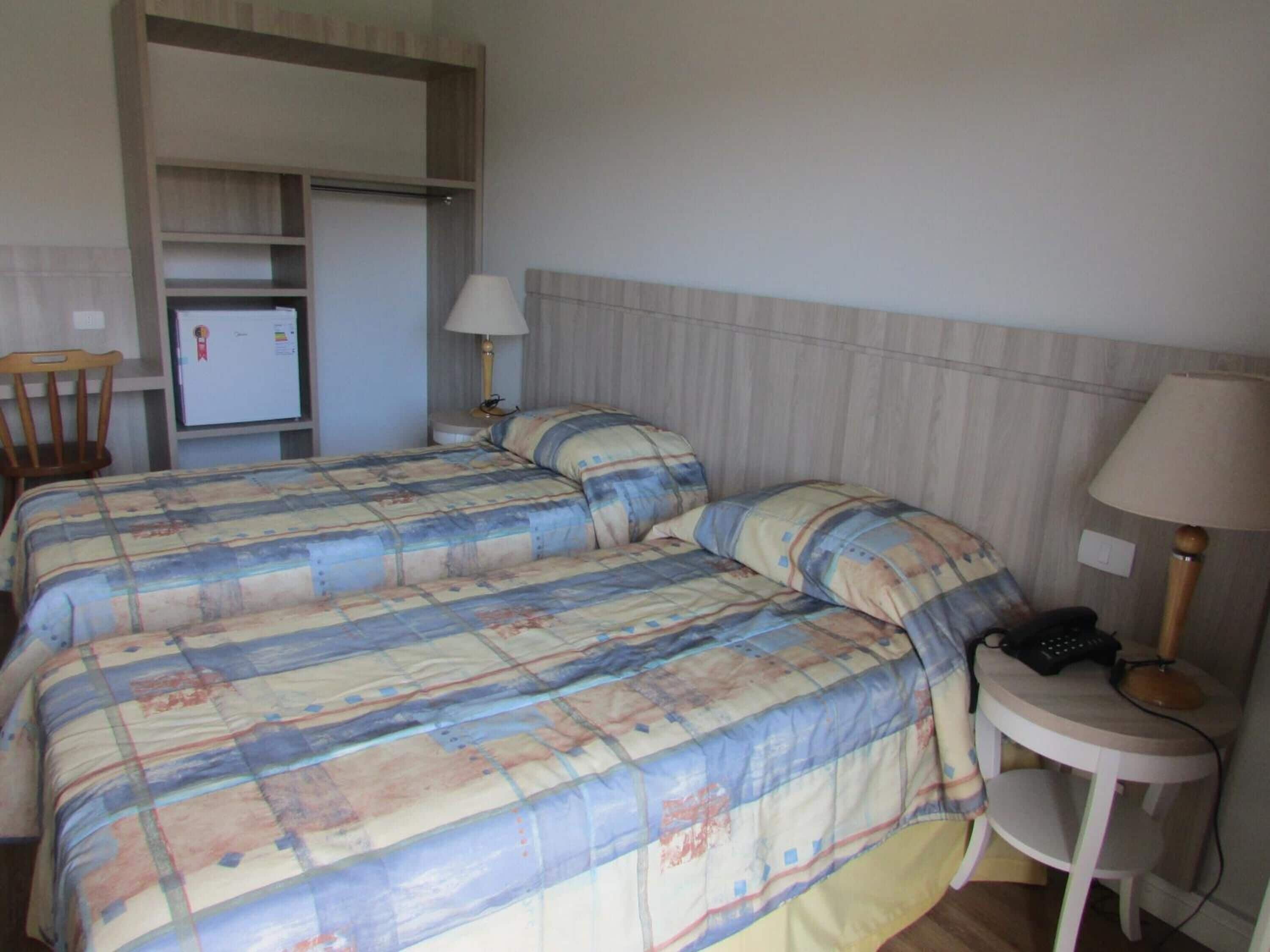 A hotel room with a bed, a desk, a chair, a lamp, and a refrigerator.