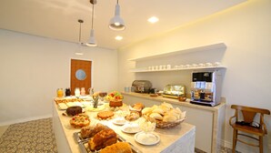 A buffet area with a variety of food items, a coffee machine, and a clock on the wall. - Moinho Itália Hotel (Campos do Jordão)