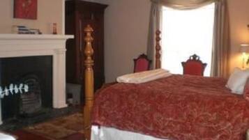 A bedroom with a large bed, a fireplace, a ceiling fan, and a window with curtains.