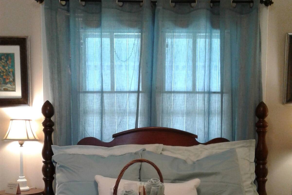 A neatly made bed with a basket of folded towels and a bedside table with a lamp.