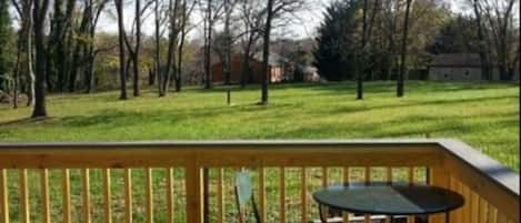 A wooden deck with a table and chairs, overlooking a grassy area with trees and a distant building.