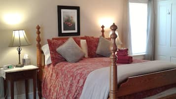 A bedroom with a wooden four-poster bed, a bedside table with a lamp, a framed picture on the wall, and a window with curtains.