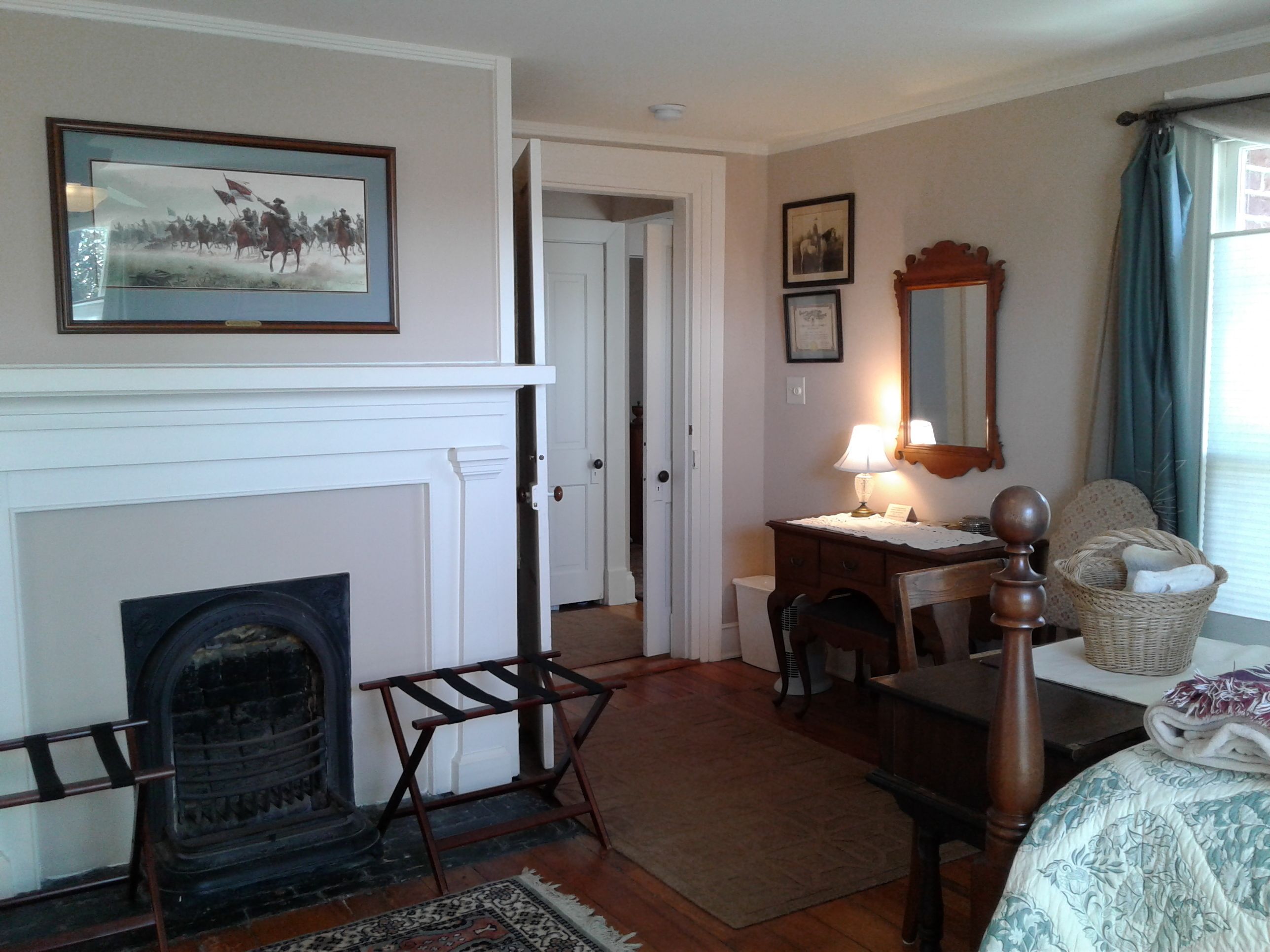 Una habitación con chimenea, un escritorio con lámpara, una silla, una cama y un espejo.