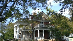 A large, two-story brick house with a wrap-around porch, columns, and a balcony. - The Boxley Place Inn (Louisa)