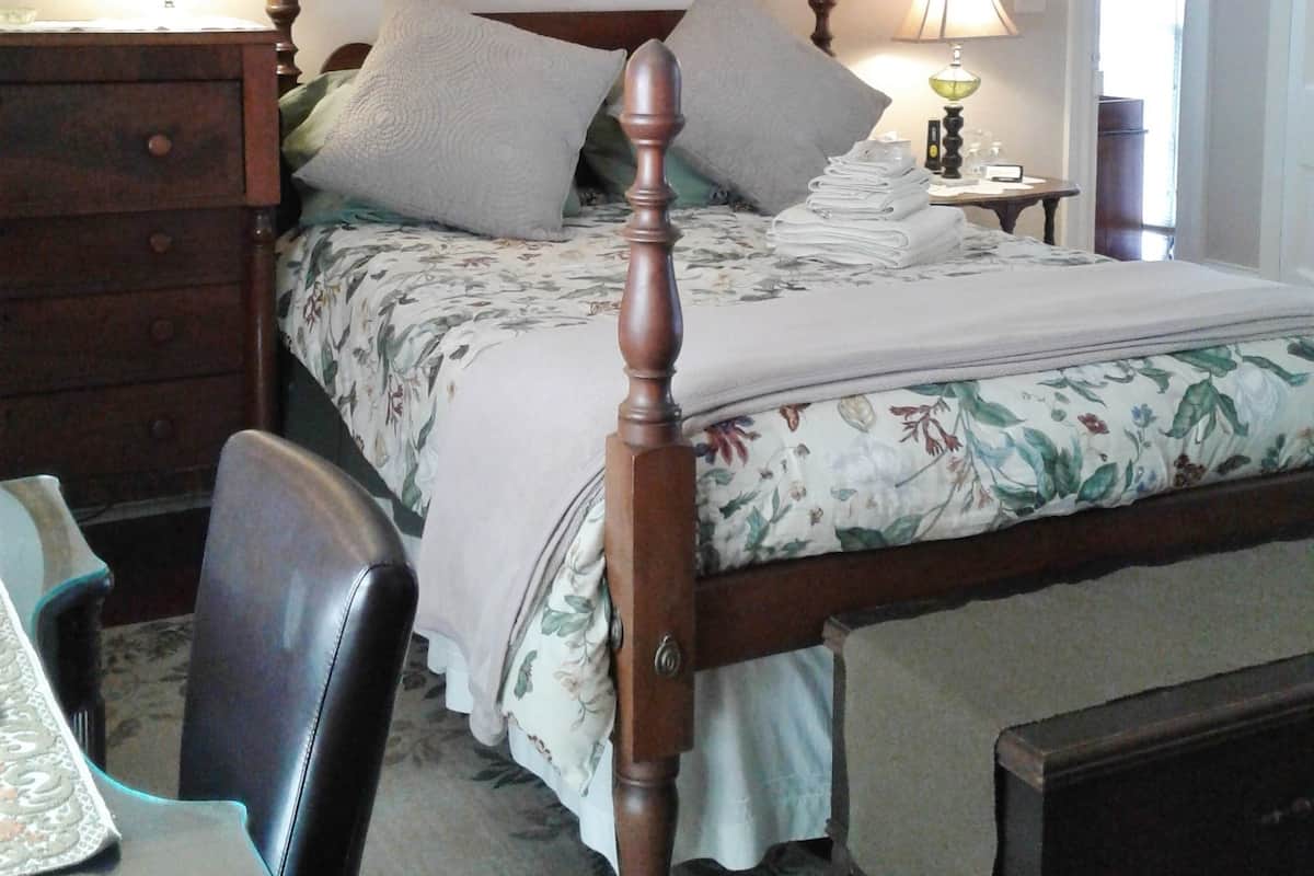 A bedroom with a wooden four-poster bed, a dresser, a chair, and a bedside table with lamps.