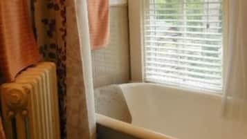 A bathroom with a bathtub, a window with blinds, and a radiator.