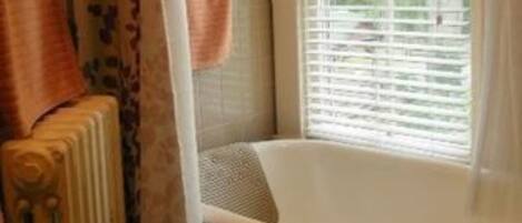A bathroom with a bathtub, a window with blinds, and a radiator.