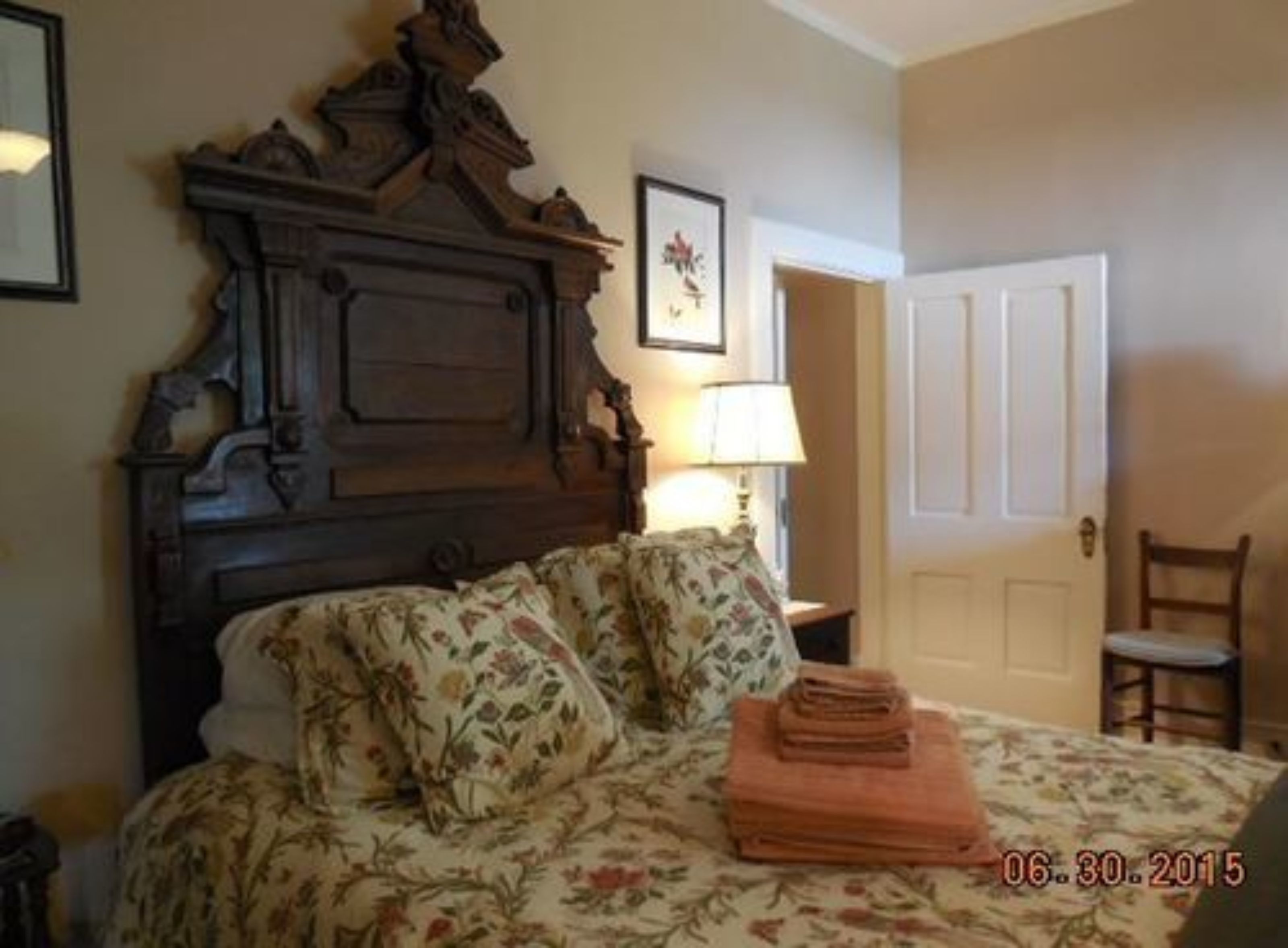 A bedroom with a wooden headboard, floral bedspread, and a lamp on a bedside table.