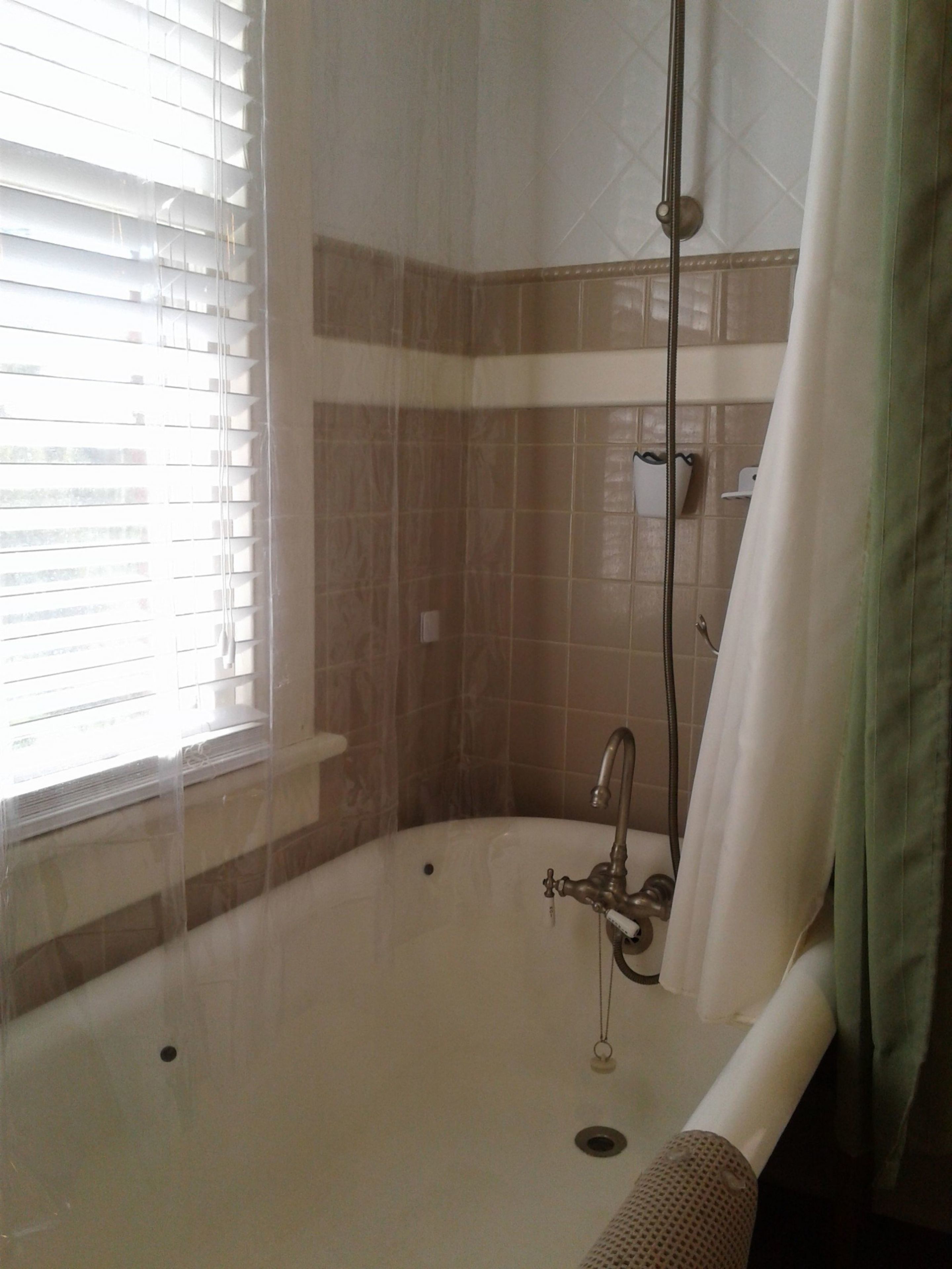 Un baño con bañera, ducha y ventana con persianas.
