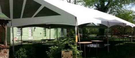 Un espace extérieur abrité, doté de tables et de chaises, et entouré de verdure et d’arbres.