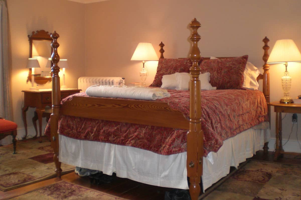 A four-poster bed with a white and red bedspread, two bedside lamps, a wooden nightstand, and a mirror on the wall.