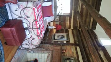 A rustic room with a bed, a red suitcase, a window, and a door with a view of a landscape.