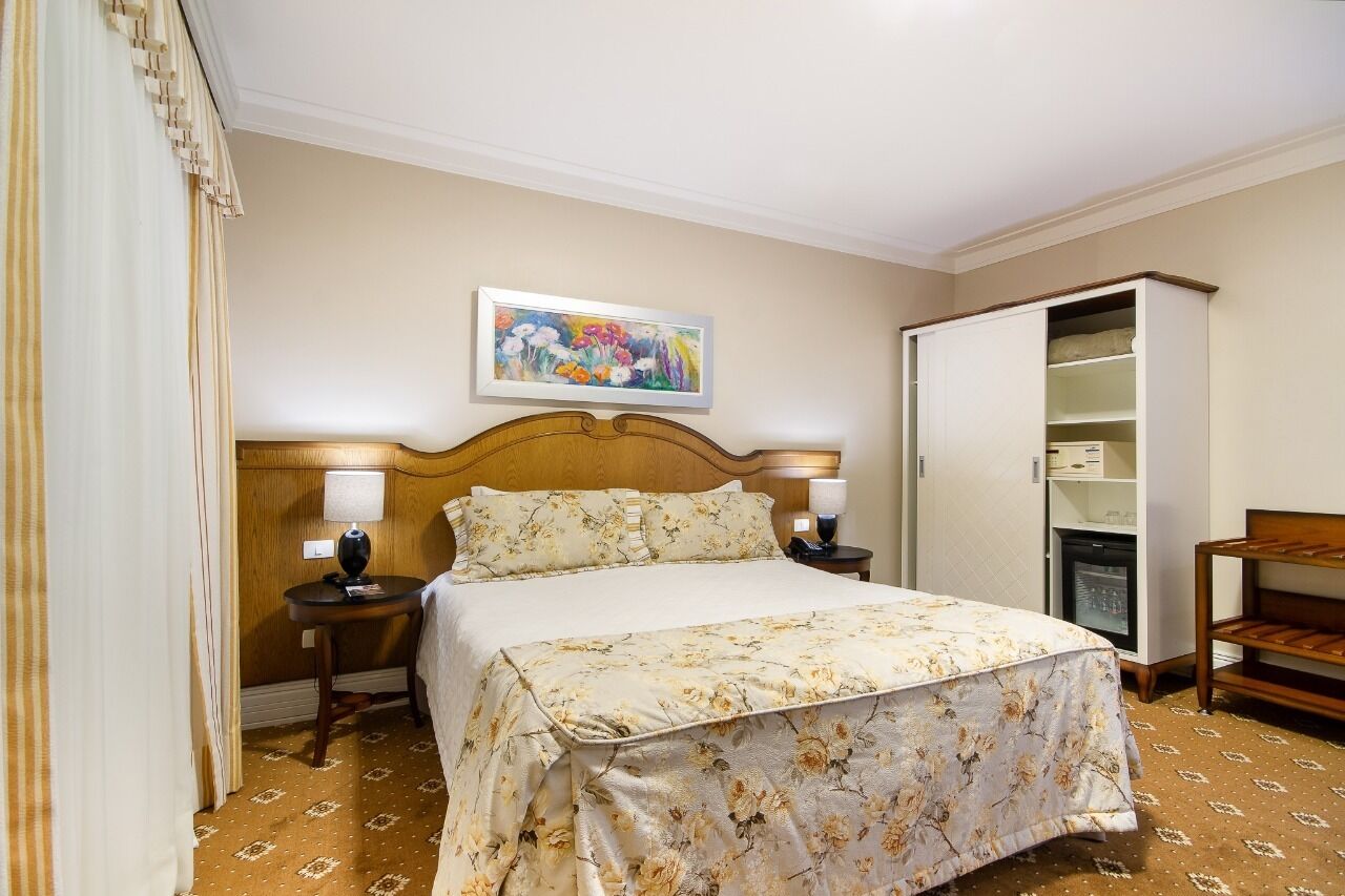 A hotel room with a bed, a nightstand, a lamp, a wardrobe, and a painting on the wall.