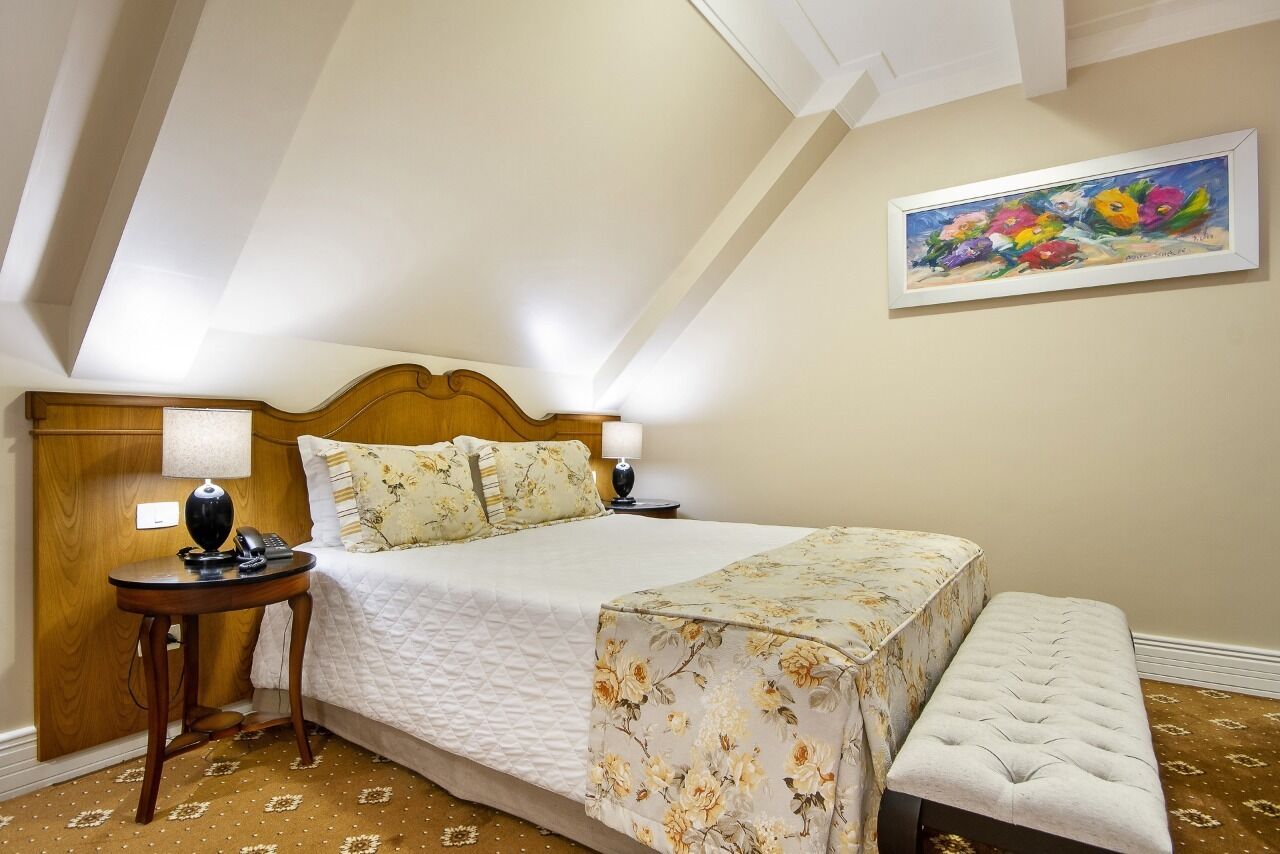 A bedroom with a bed, bedside tables, a bench, and a painting on the wall.