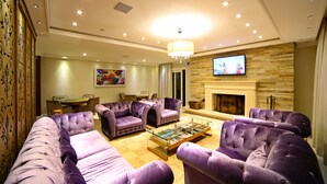 A modern living room with a fireplace, plush purple sofas, a coffee table, and a television mounted on the wall. - Pousada Italia Eleganza (Campos do Jordão)
