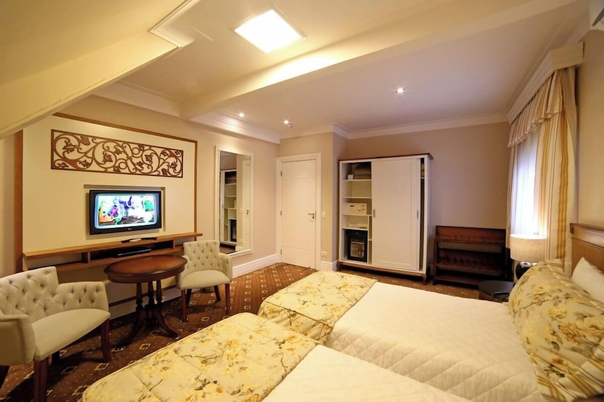 Una habitación de hotel con una cama, dos sillones, un televisor, un armario y una pequeña mesa.