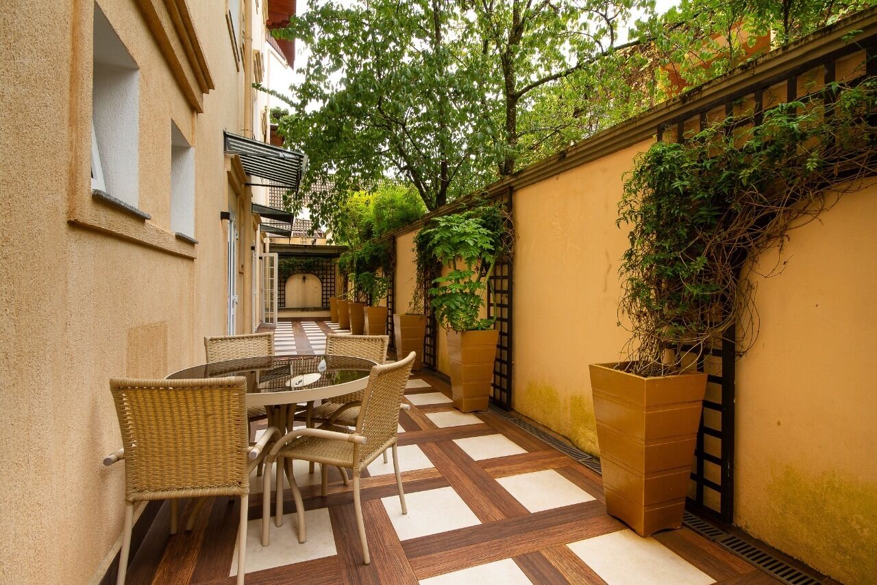 Un patio con una mesa redonda y sillas, rodeado de un suelo de baldosas y una pared cubierta de plantas trepadoras.