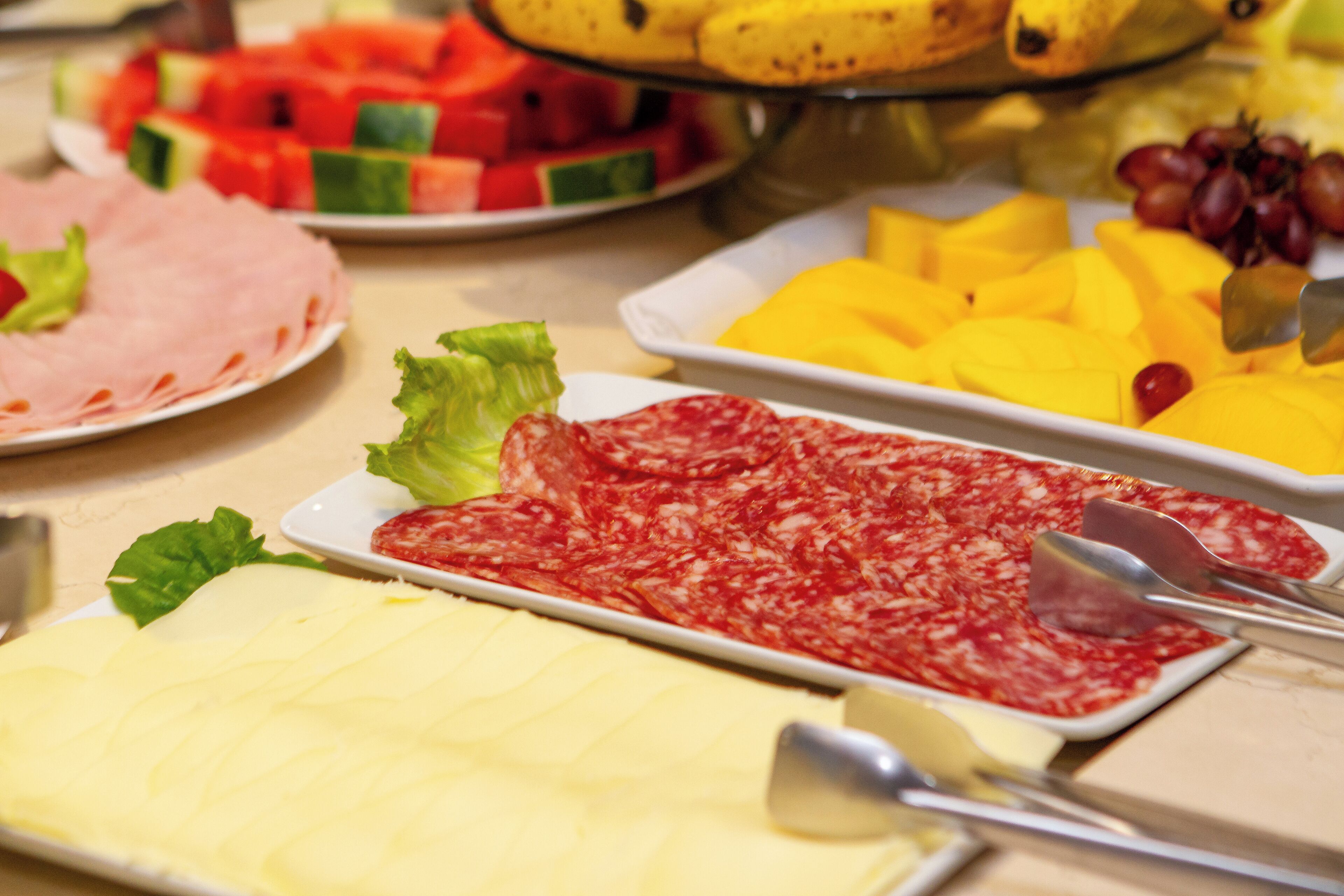 A buffet with various food items including sliced ham, cheese, and fruits like watermelon and mango.