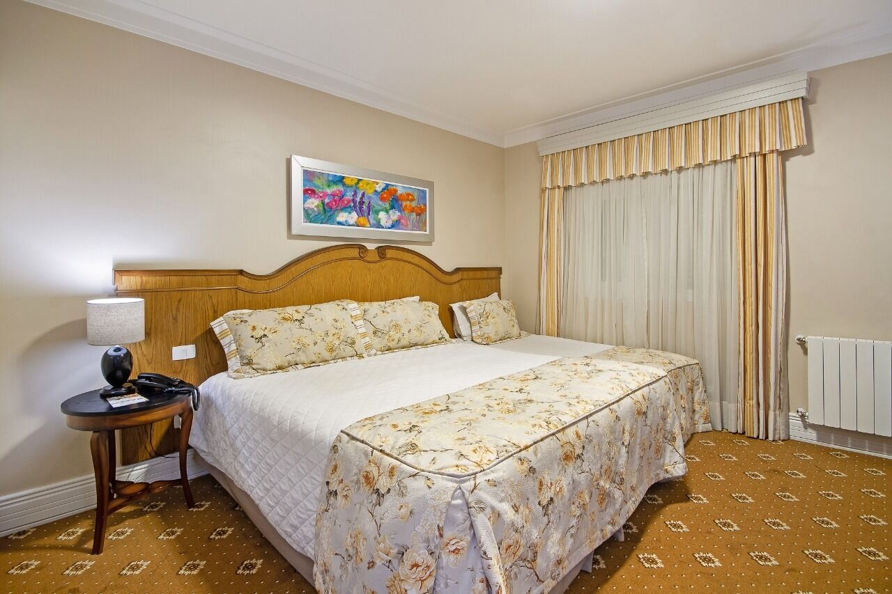 Ein Hotelzimmer mit einem großen Bett, einem Nachttisch mit Lampe, einem Bild an der Wand und einem Fenster mit Vorhängen.