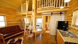 L’intérieur d’une cabane en rondins, avec un escalier en bois, un canapé, une table à manger et un coin cuisine.