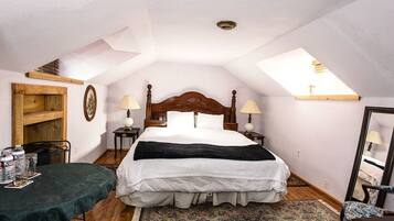 A bedroom with a large bed, two bedside tables, a wooden headboard, a skylight, a small table with chairs, and a patterned rug.