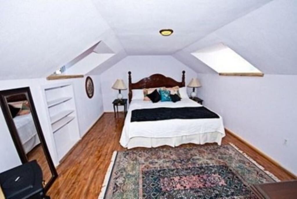 A bedroom with a bed, two bedside lamps, a rug, and a skylight.