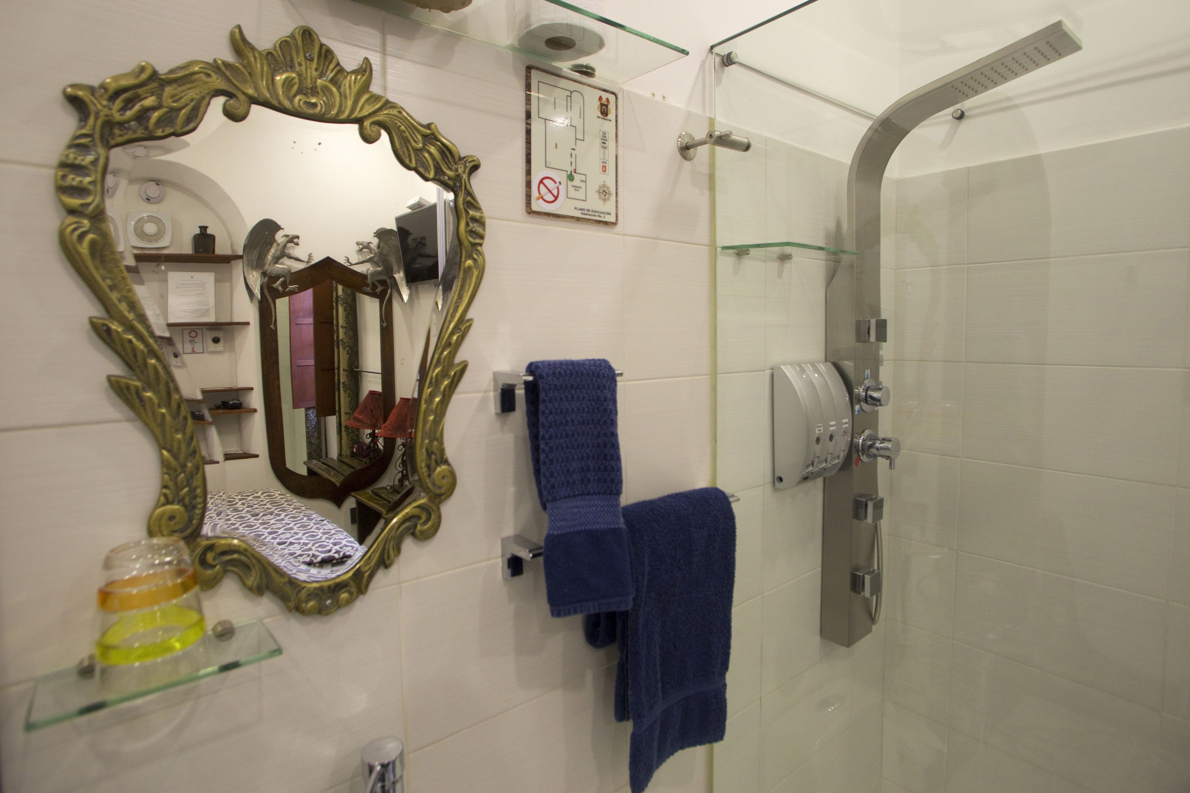 A bathroom with a large ornate mirror, a glass shower enclosure, and two blue towels on a rack.