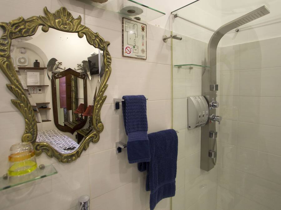 A bathroom with a large ornate mirror, a glass shower enclosure, and two blue towels on a rack.