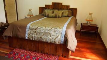 A wooden bed with a patterned bedspread, two bedside lamps, and a red patterned rug on a wooden floor.