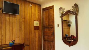 A room with wooden paneling, a wooden door, a television mounted on the wall, and a mirror with a decorative frame.