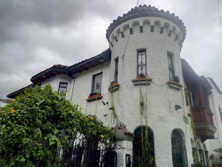A white building with a round tower, multiple windows, and a balcony with plants.