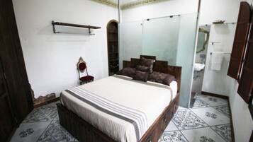 A bedroom with a large bed, a wardrobe, a mirror, and a bathroom visible through an arched doorway.