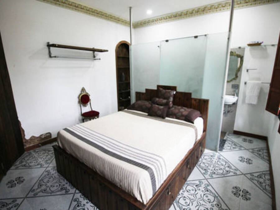 A bedroom with a large bed, a wardrobe, a mirror, and a bathroom visible through an arched doorway.