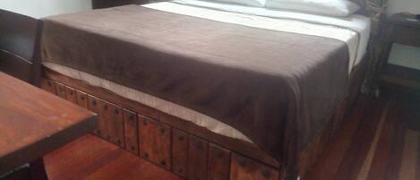 A room with a bed, a wooden table, and a window with curtains.