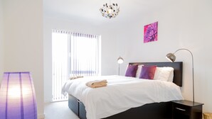 Een slaapkamer met een bed, nachtkastjes, een lamp, een raam met zonwering en een kunstwerk aan de muur.