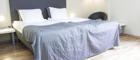 A modern bedroom with a large bed, a bedside table, a chair, and a floor lamp.