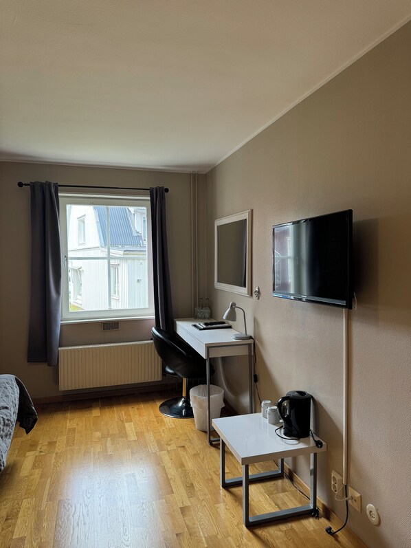 A hotel room with a wooden floor, a desk with a chair, a TV, and a window with curtains. - Ullångers Hotell och Restaurang (Ullanger)