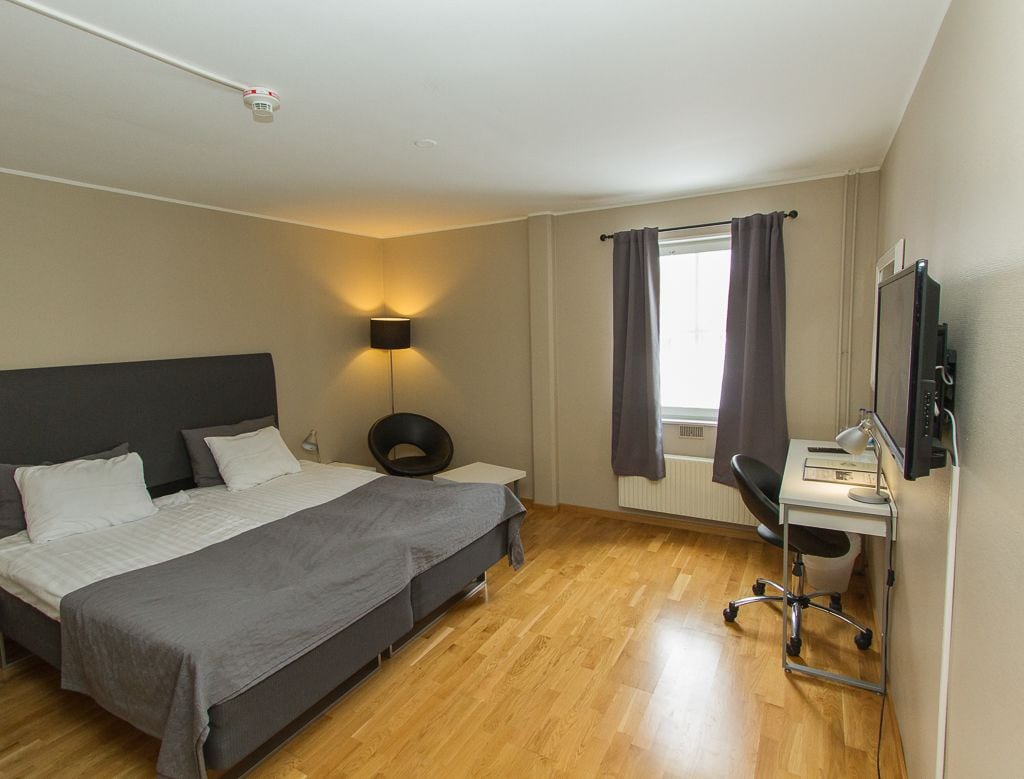 Habitación de hotel con cama, escritorio, silla, lámpara y televisor.