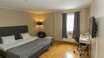 Habitación de hotel con cama, escritorio, silla, lámpara y televisor.