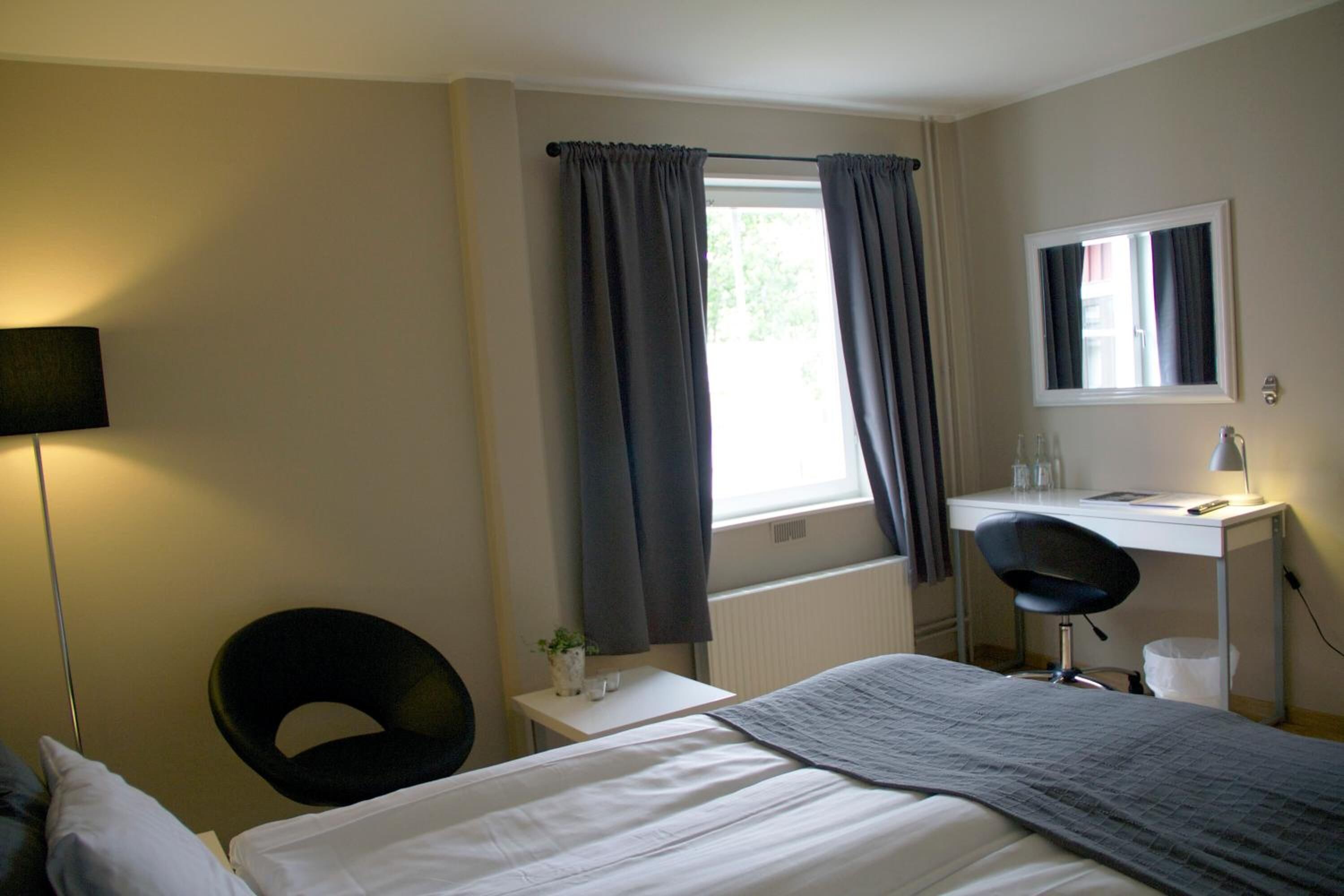 Una habitación de hotel con una cama, un escritorio con una silla, una lámpara y una ventana con cortinas.