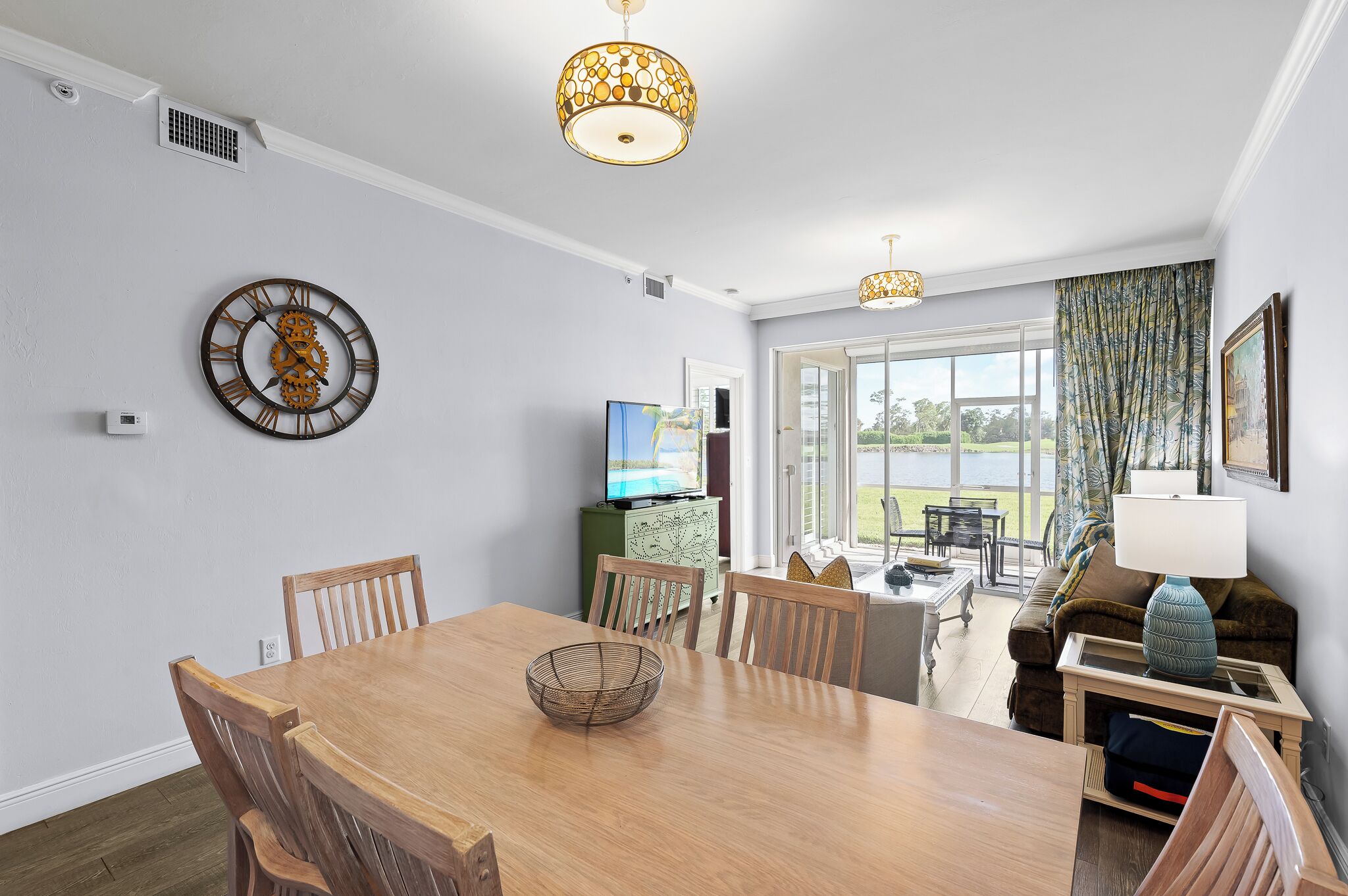 A dining area with a wooden table and chairs, a decorative clock, and a television in the background.
