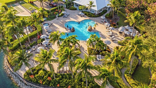 Vista aérea de un resort con piscina central, palmeras y zona de playa.