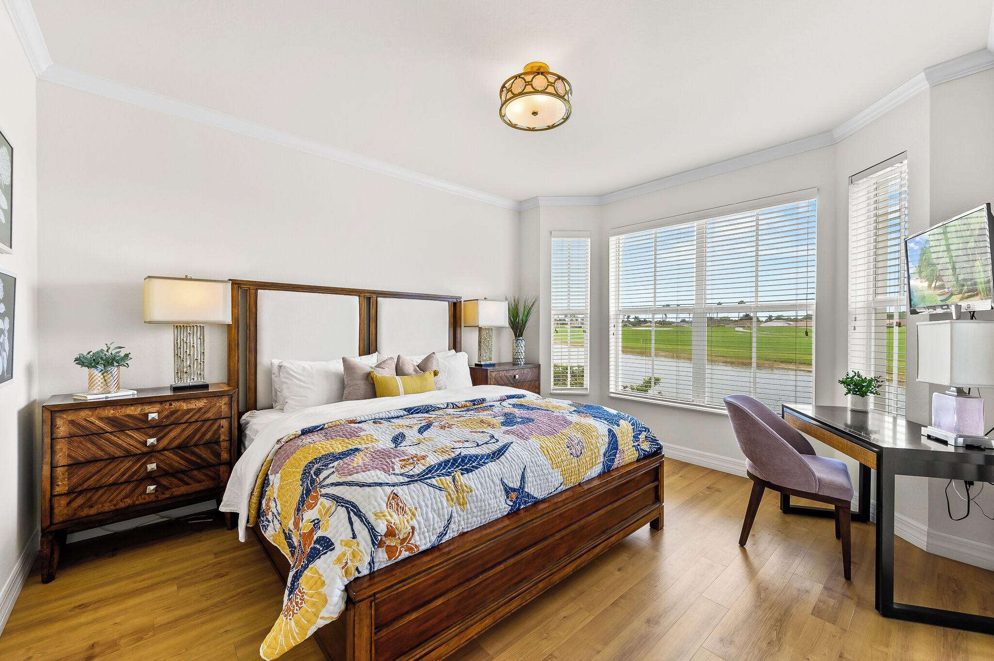 A bedroom with a wooden bed, a desk with a chair, and large windows with blinds.