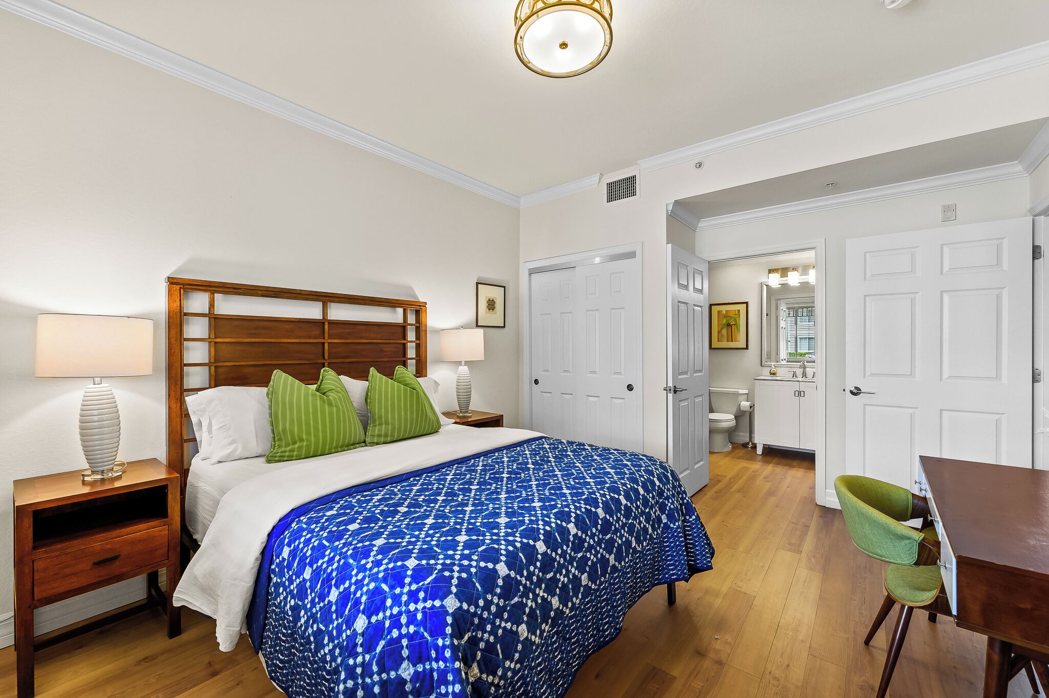 Ein Hotelzimmer mit einem großen Bett, einem Holzkopfteil, zwei Nachttischen mit Lampen, einem grünen Sessel und einem kleinen Tisch.