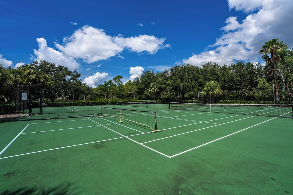 Ulkotenniskenttä, jossa on useita kenttiä, ja sen ympärillä on puita ja avoin, kirkas taivas.