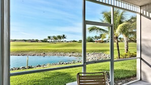 Vista desde una ventana sobre un campo de golf con un estanque y palmeras.