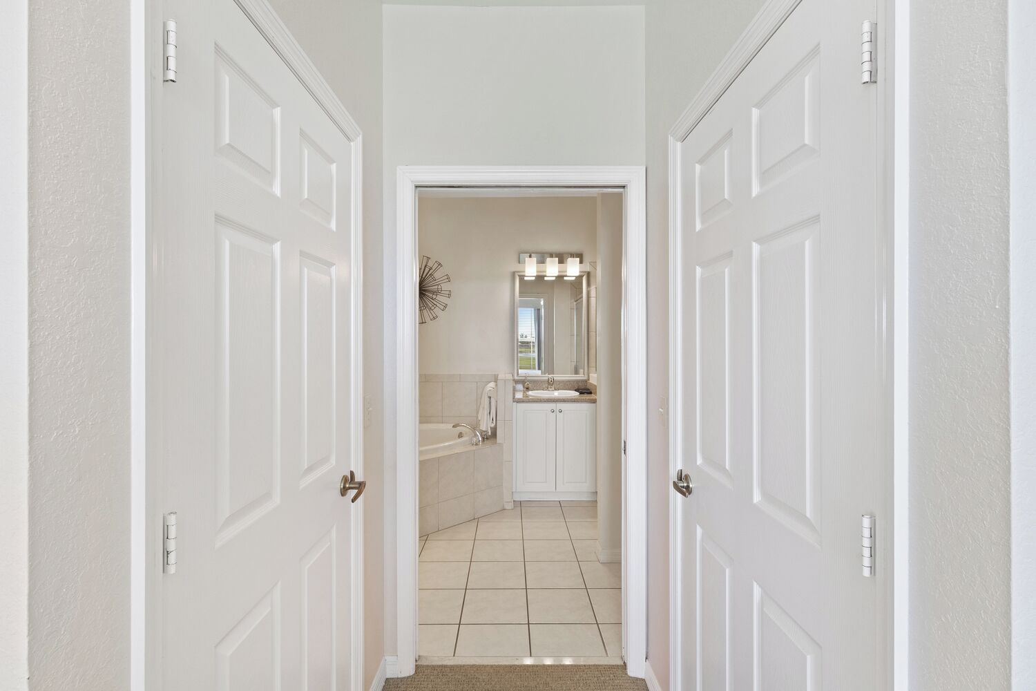 A hallway leading to a bathroom with a sink, mirror, and light fixture.